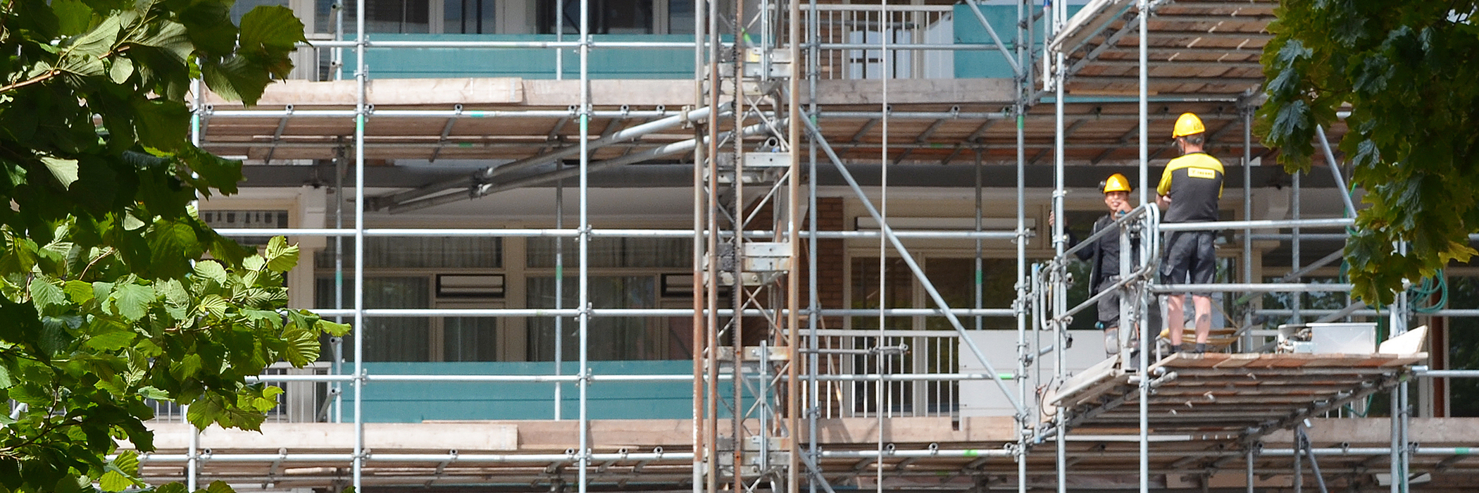 Flatgebouw in de stijgers. op de stijger staan twee mannen in werkkleding met een gele helm op.