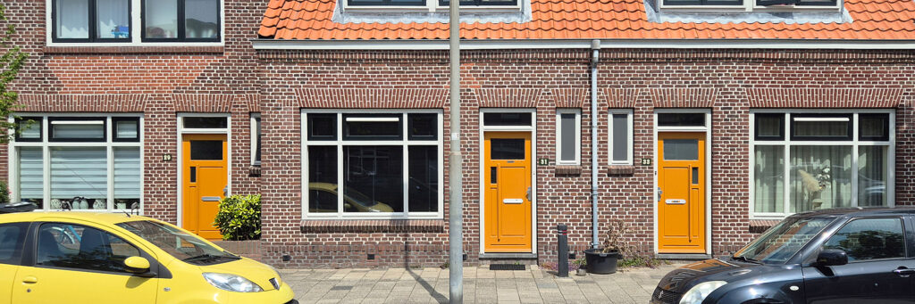 schakelwoning met gele/ oranje deuren. ervoor zijn parkeerplekken met autos