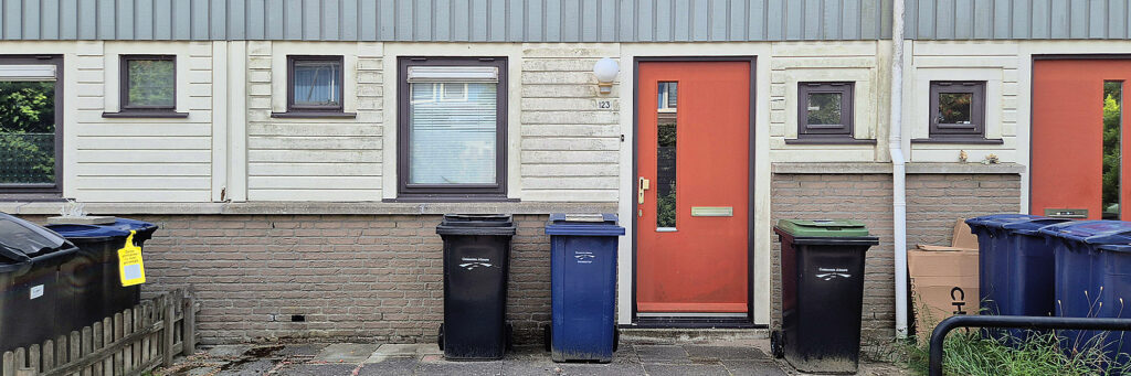 entree van een woning, voor de deur staan drie containers. de deur is rood en de rest van de woning wit