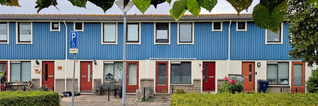 woningen met rode deuren, witte kozijnen en de bovenverdieping is blauw. voor het complex is een groene struik