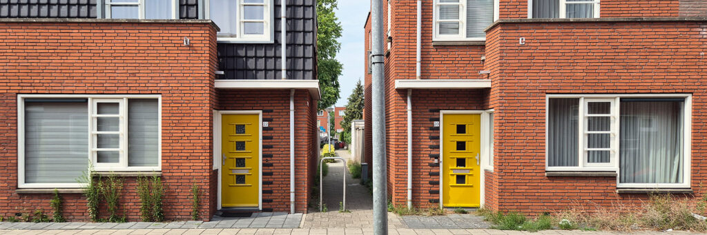 Woningen met een gangetje ertussen. de woningen zijn bruin met witte kozijnen en hebben gele deuren