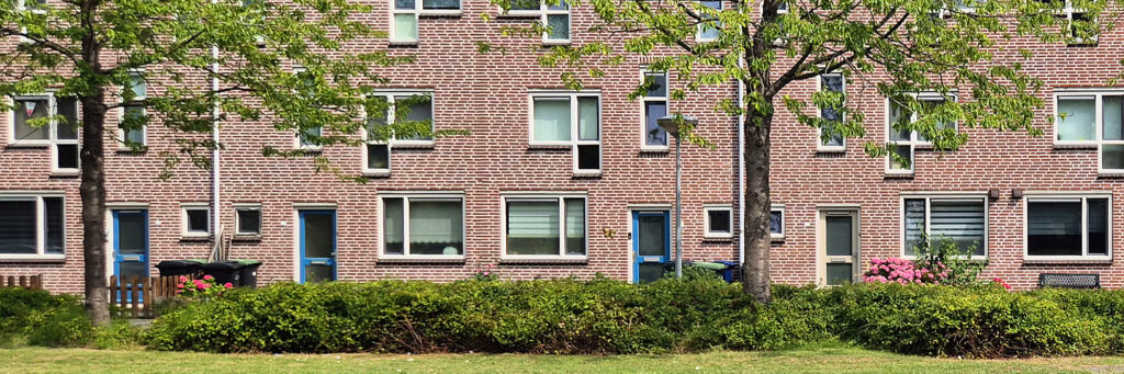 schakelwoningen met blauwe deuren en een groenstrook met bomen