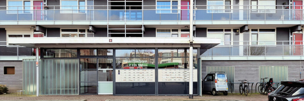 flatgebouw met bij de entree een fietsenrek en een parkeergelegenheid. het complex is voornamelijk wit en heeft rode deuren