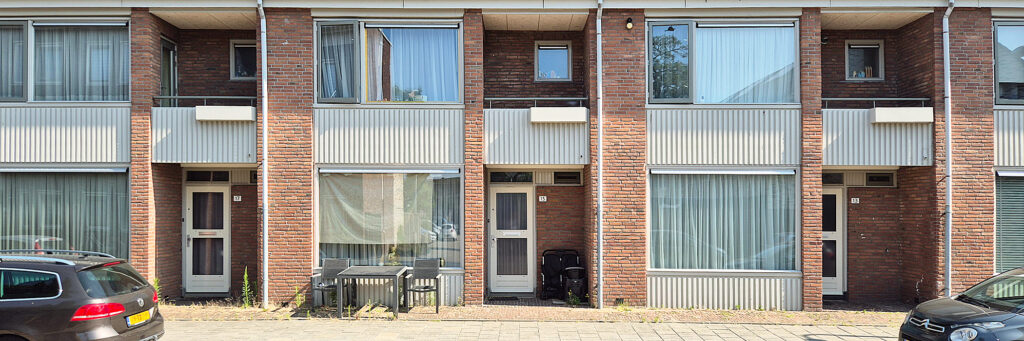 entree van een aantal woningen met balkon, op de stoep staan stoelen en een tafel en ervoor is parkeergelegenheid