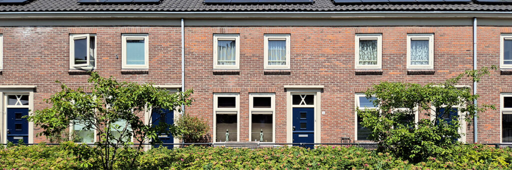 Rijtjeshuizen met blauwe deuren en witte kozijnen. ervoor is een groen struik die in de volledige breedte doorloopt