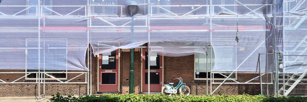 Woningen die worden verbouwd, het complex staat in de stijgers. en voor de deur staat een kinderfietsje