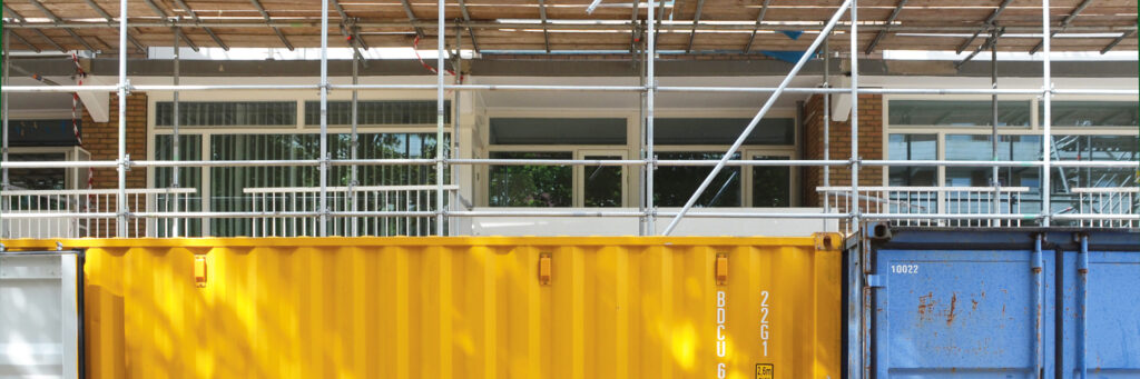 woning die in de stijgers staat. voor de woning staat een gele en blauwe afvalcontainer