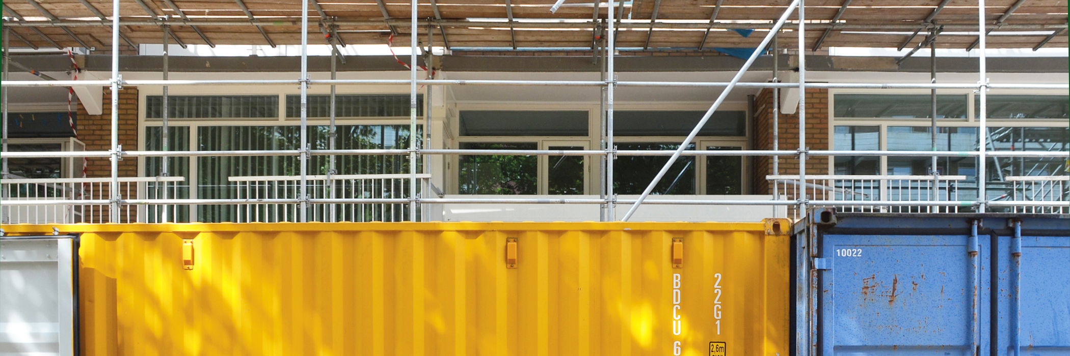 woning die in de stijgers staat. voor de woning staat een gele en blauwe afvalcontainer