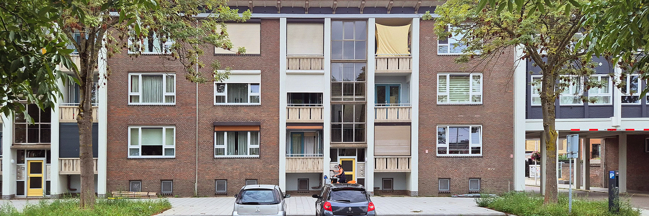 entree van een appartementen complex met witte kozijnen ervoor is parkeergelegenheid