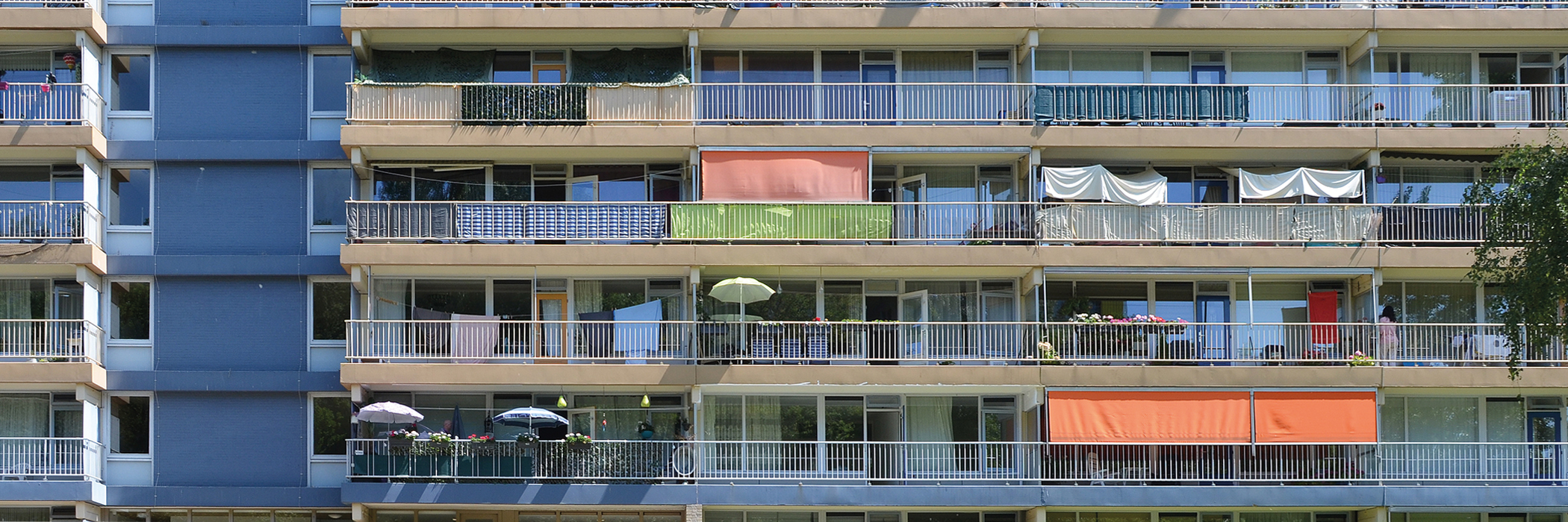 flatgebouw met als basiskleur blauw en beige. de zonnewering die uithangt bij een aantal is rood