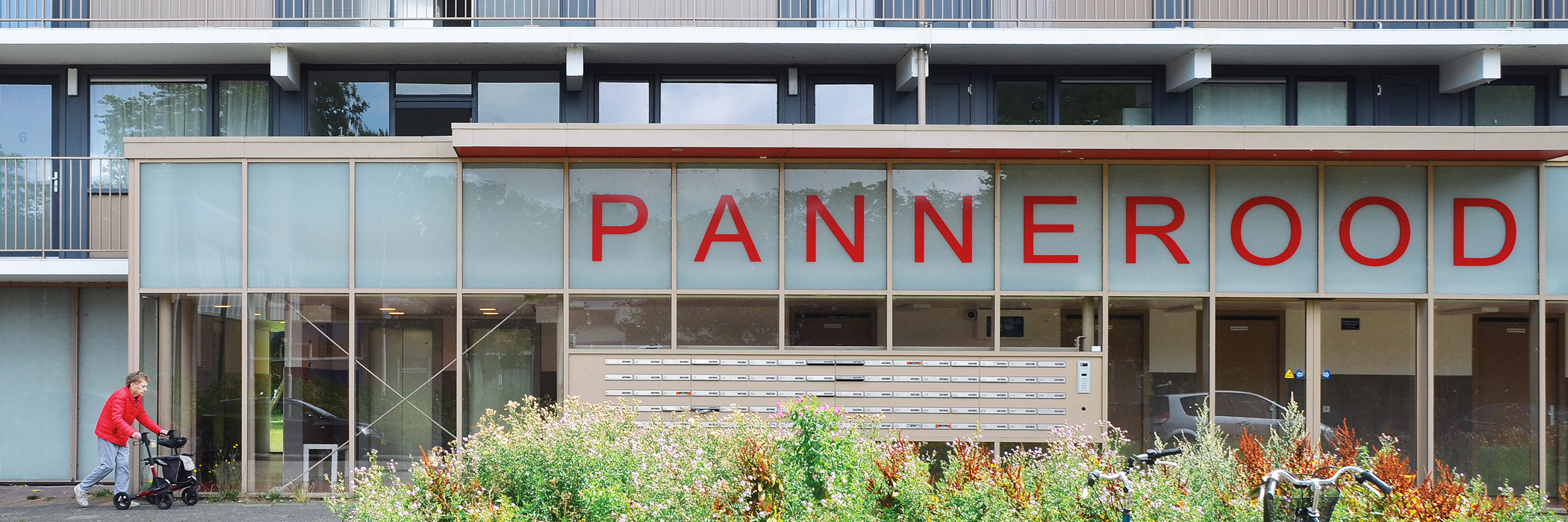 flatgebouw met brievenbussen aan de buitenkant, daarboven staat in het rood de naam van het complex