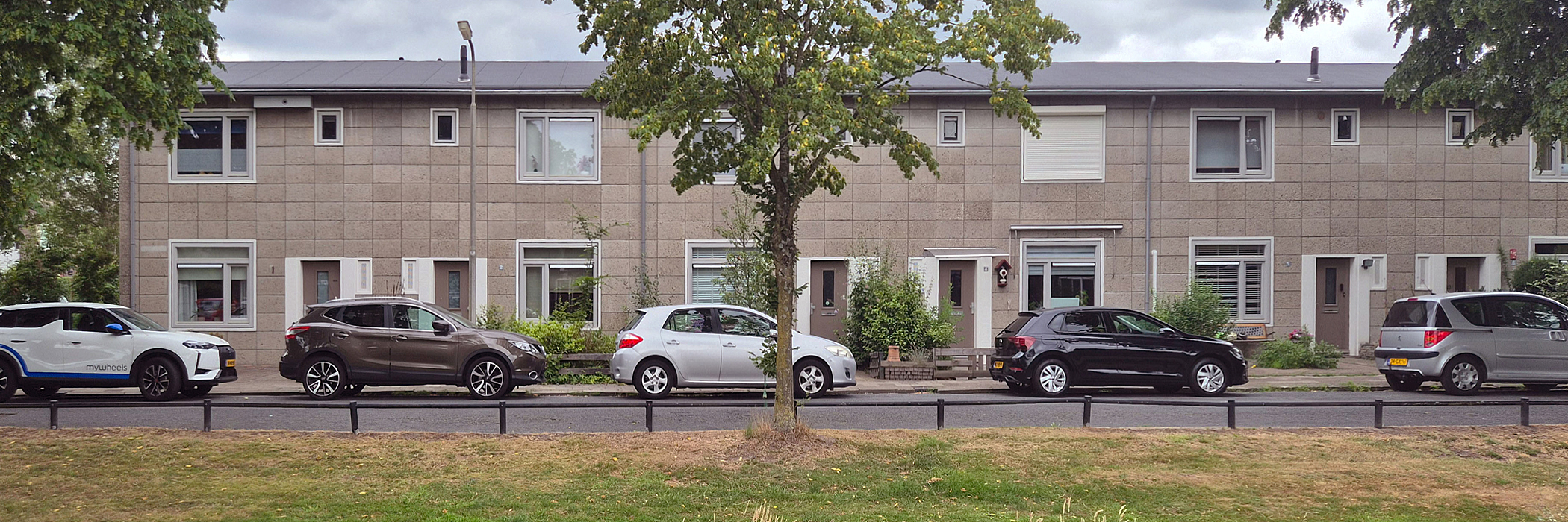 rijtjeswoningen met autos voor de woningen. daarvoor is een groenstrook met een boom