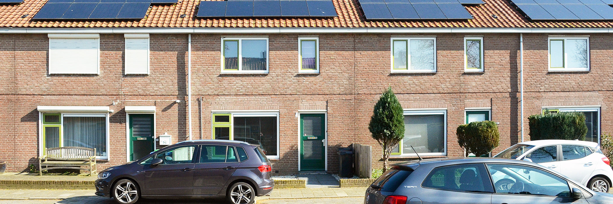 rijtjeswoningen met groene deuren witte kozijnen en groene ramen. voor de woningen zijn parkeerplekken