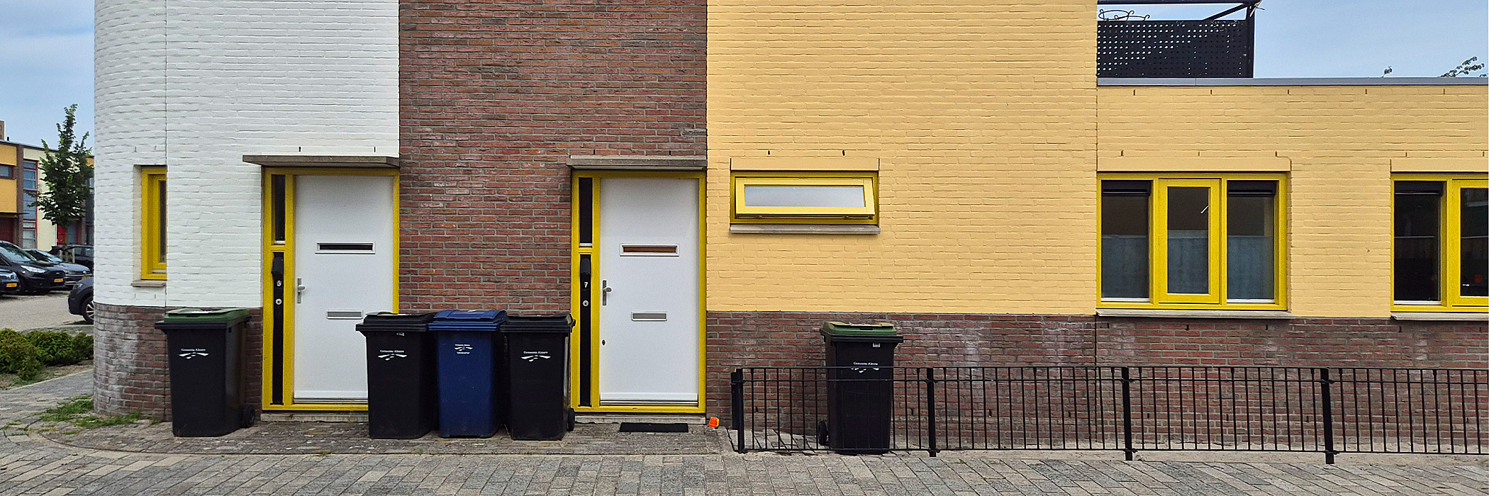 wonning die aan de rechterkant geel is met gele kozijnen. ze hebben witte deuren