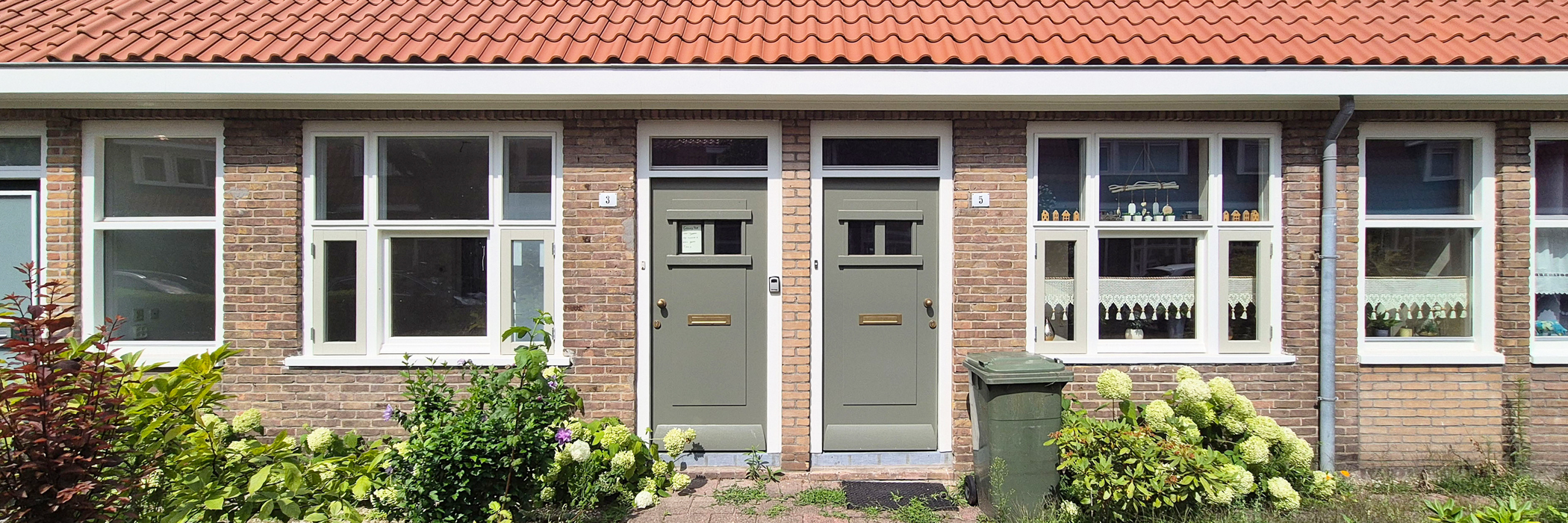 schakelwoning met groenige deuren en witte kozijnen. voor de deur staat een container