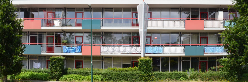 flatgebouw met rood groen en wit. ervoor staan een groene struik