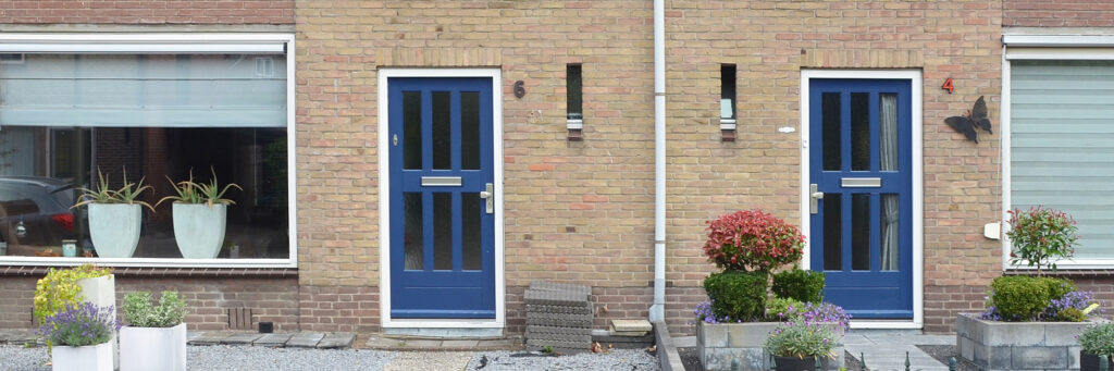 Woningen met blauwe deuren en in de voortuin plantenbakken met gekleurde planten erin