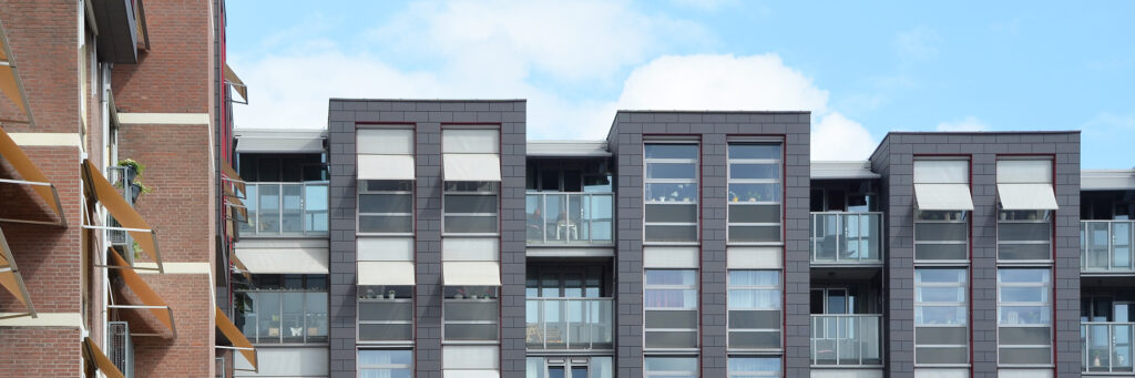 Nieuwere appartementen met grijze stenen en witte kozijnen. de zonwering hangt eruit en is ook wit