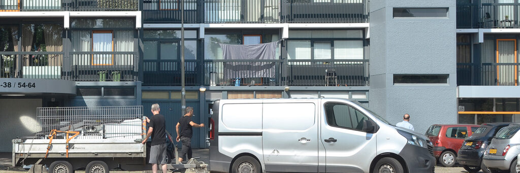 flatgebouw waar een werkbus met aanhanger met een hoop spullen erop