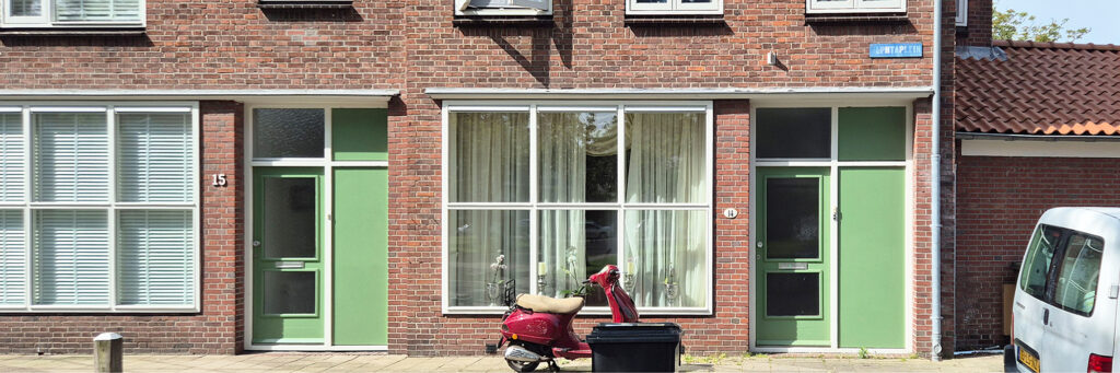 woningen met groenen deuren en bruine stenen, er staat een rode scooter voor de deur