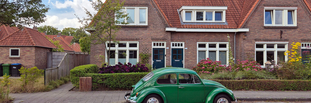 Woningen met mooie tuinen met paars roze geel en groen, voor het huis staat een groene beetle