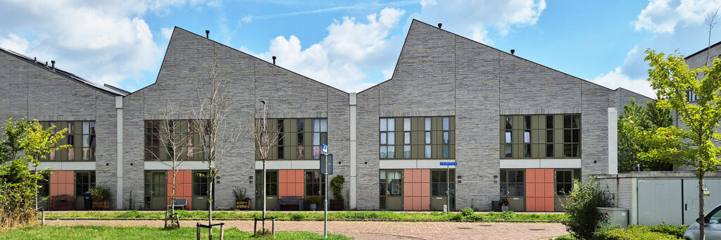 woningen die de vorm hebben van een oude loods, de kleur is grijs met groenen en oranje vlakken. het ligt gelegen aan een weg