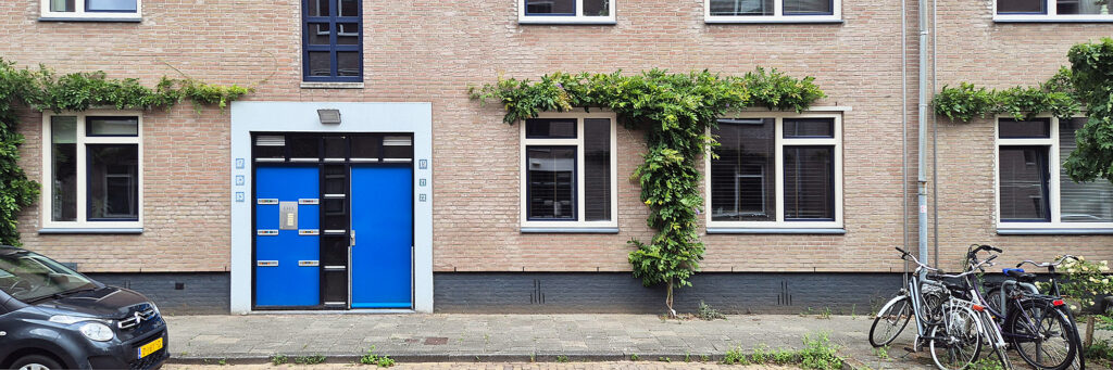 entree van woningcomplex. de deur is blauw en voor de deur is er parkeergelegenheid en staan een aantal fietsen