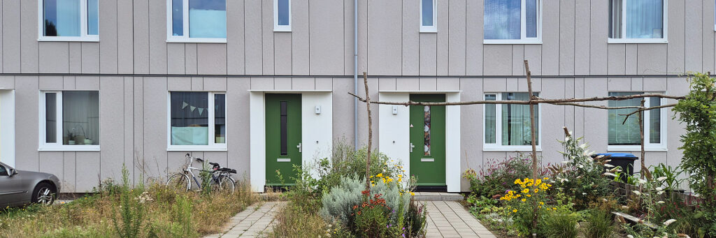 Grijze woningen met groenen deuren. ertussen zijn groene stroken met kleurrijke planten