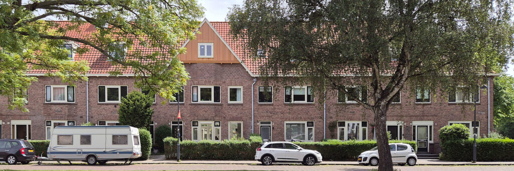 rijtjeswoning met struiken ervoor. aan de weg staan auto geparkeerd en een caravan